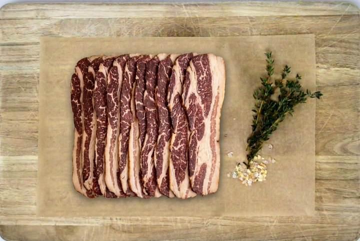 Uncooked beef bacon slices on parchment over a pale wooden cutting board.
