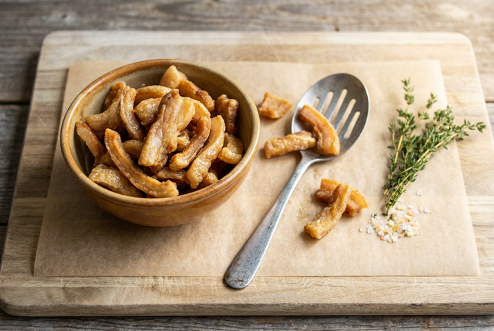Golden pork cracklings in a rustic bowl on parchment on a wooden cutting board.