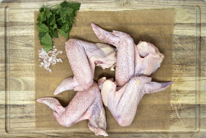 Raw chicken wings on parchment with herbs on a wooden cutting board with its outline visible.