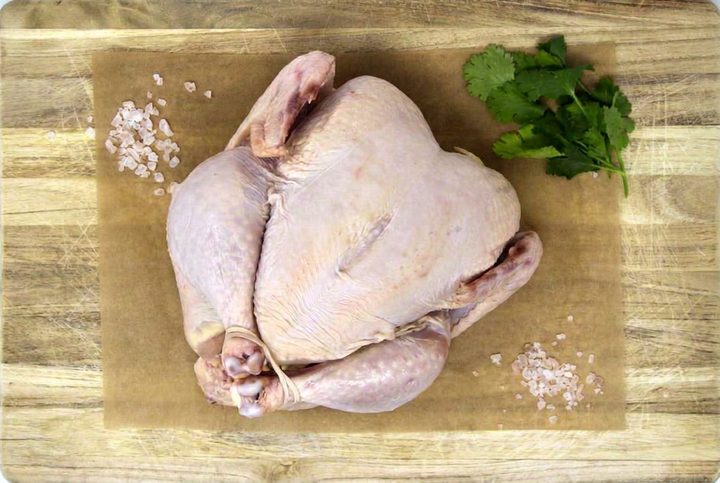 Raw whole chicken with herbs on a wooden cutting board, with the board outline visible.