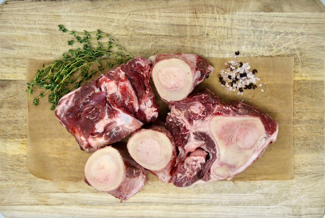 Raw beef soup bones with herbs and seasoning on a wooden cutting board with its outline visible.